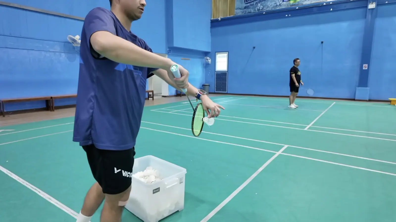 Joueur au service avec une boîte de volants : le service coupé au badminton