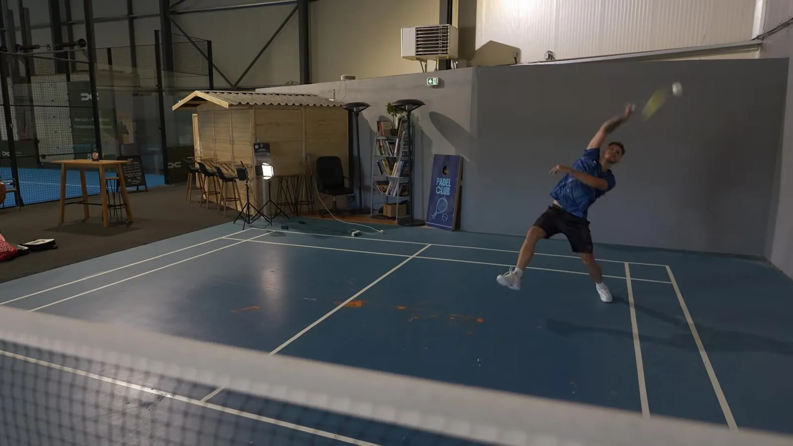 Richard Badminton saute pour frapper un volant haut au-dessus de sa tête, filmé depuis l'autre côté du filet