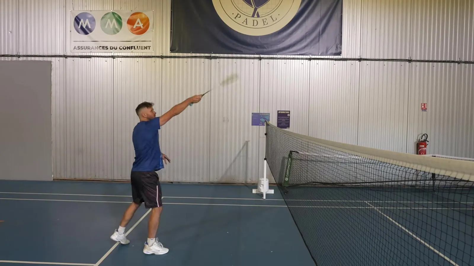 Richard Badminton près du filet, bras levé devant lui pour frapper le volant avec un geste court