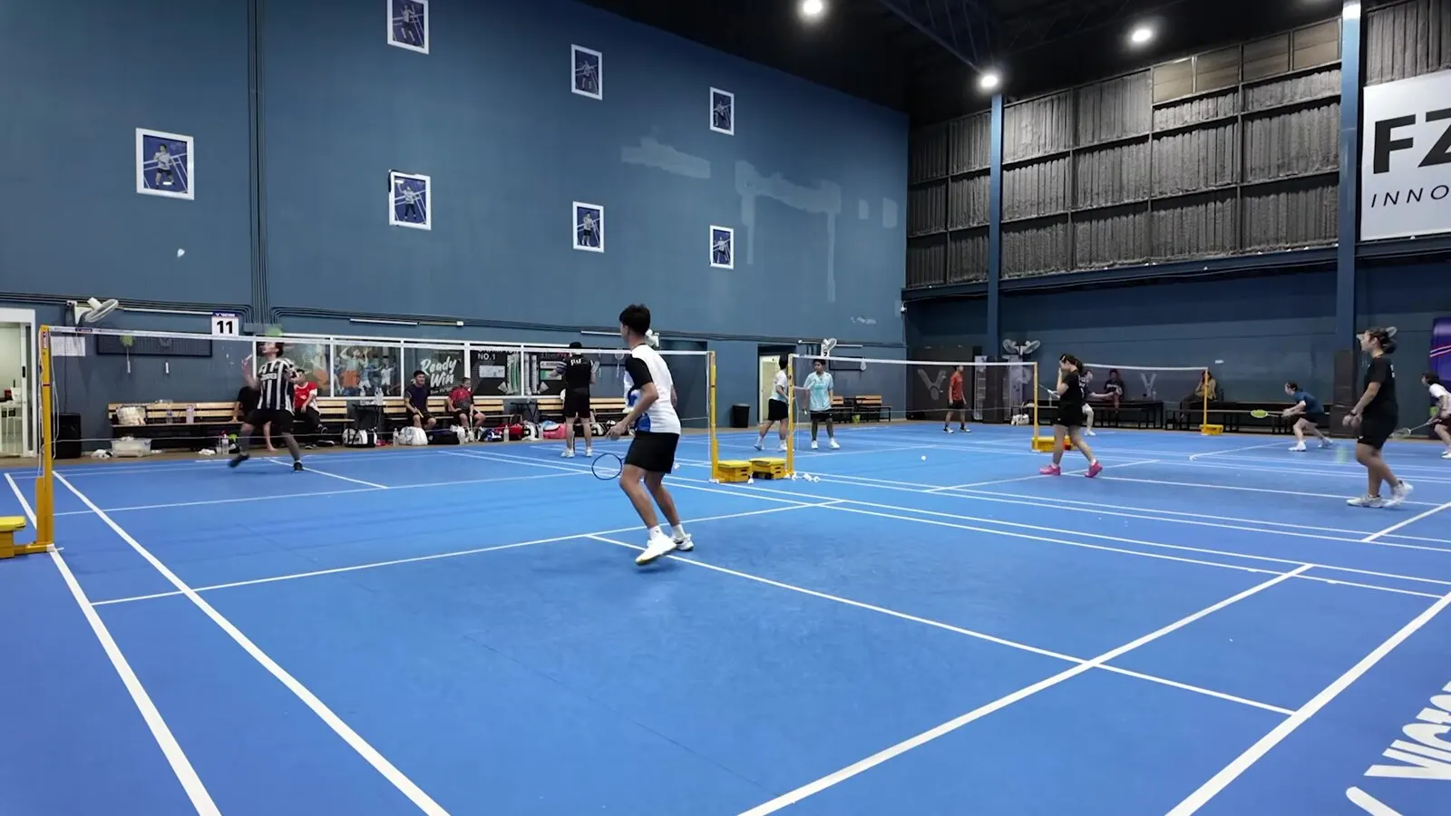 Joueur en mouvement au centre du terrain pendant un échange, dans une grande salle de badminton