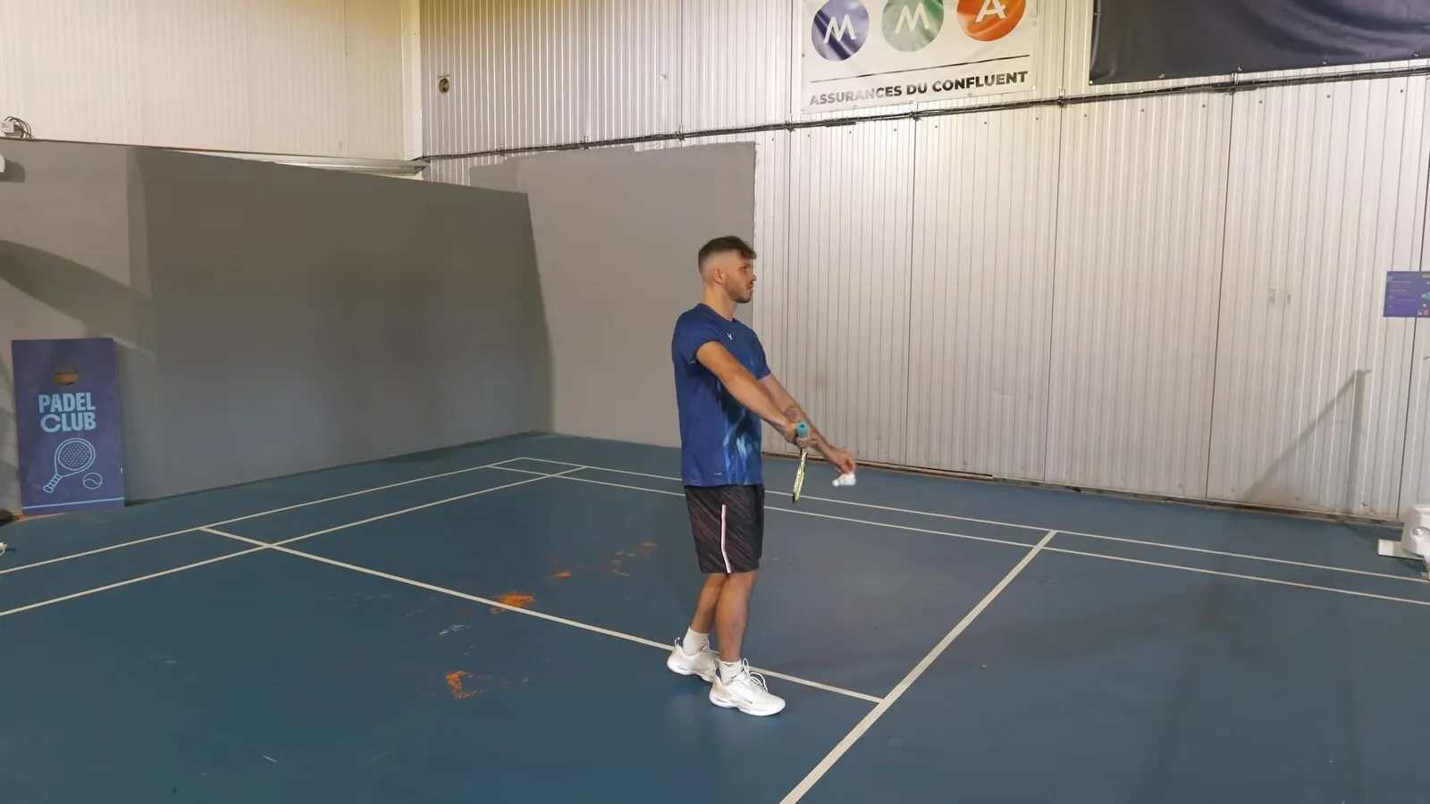 Richard Badminton en position de service, volant tenu devant lui, au moment de servir sur un terrain de club