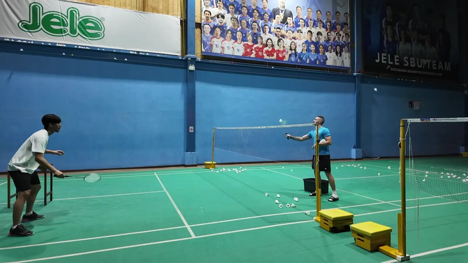 Exercice de défense au badminton : joueur à mi-court, raquette devant lui, face à un coach qui envoie des volants