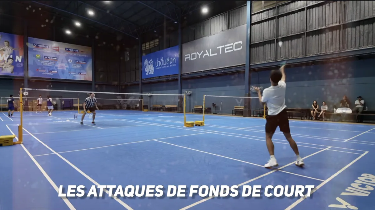 Gestes techniques du badminton en fond de court : joueur en position de smash armé au-dessus de la tête sur un terrain de badminton