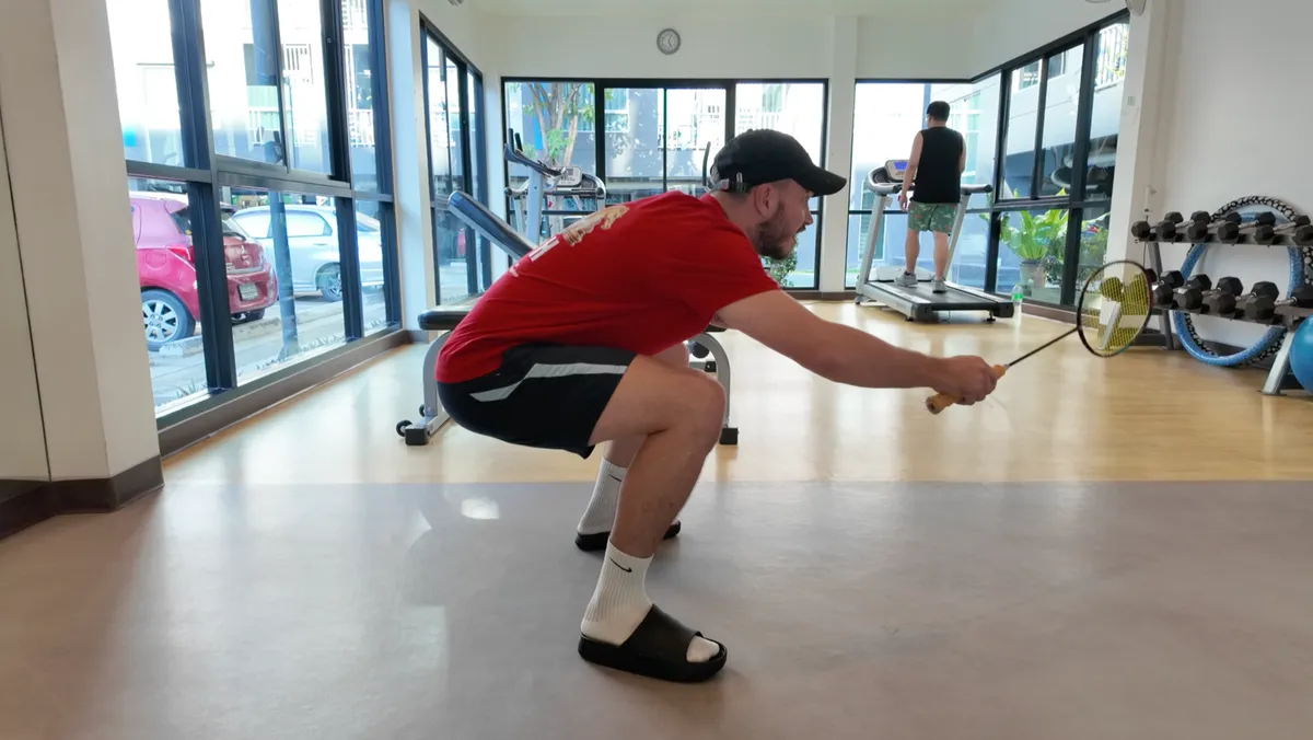 Posture basse en badminton : joueur en position fléchie avec raquette tendue dans une salle de sport à Bangkok