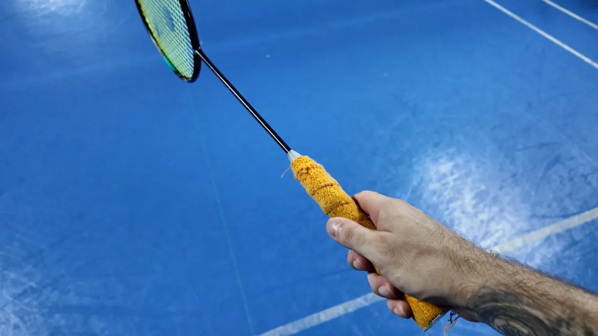 Prise de raquette badminton : main tenant un grip éponge sur un terrain de badminton bleu