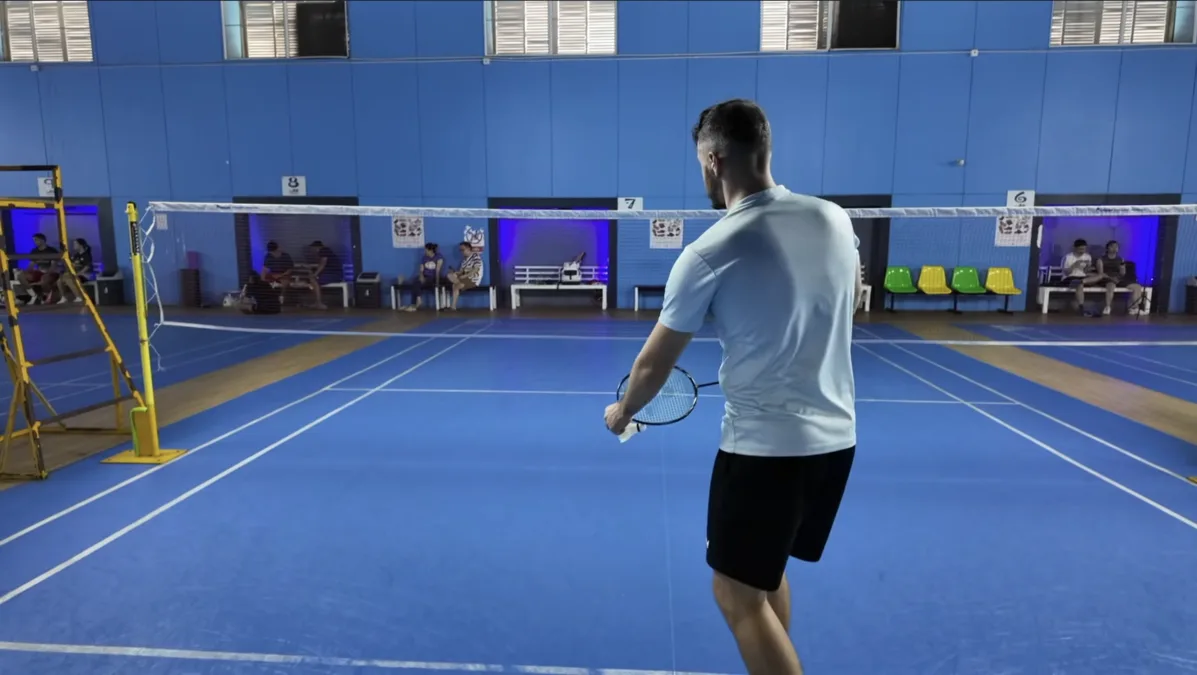 Posture de service revers au badminton : position des pieds près de la ligne, poids du corps vers l'avant, regard sur la bande du filet