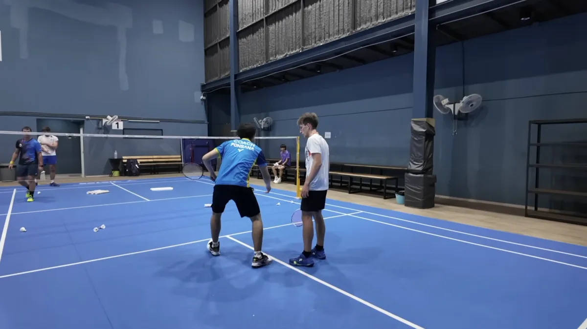 Coaching individuel au stage badminton Bangkok : un coach thaïlandais corrige la technique d'un joueur français sur le terrain