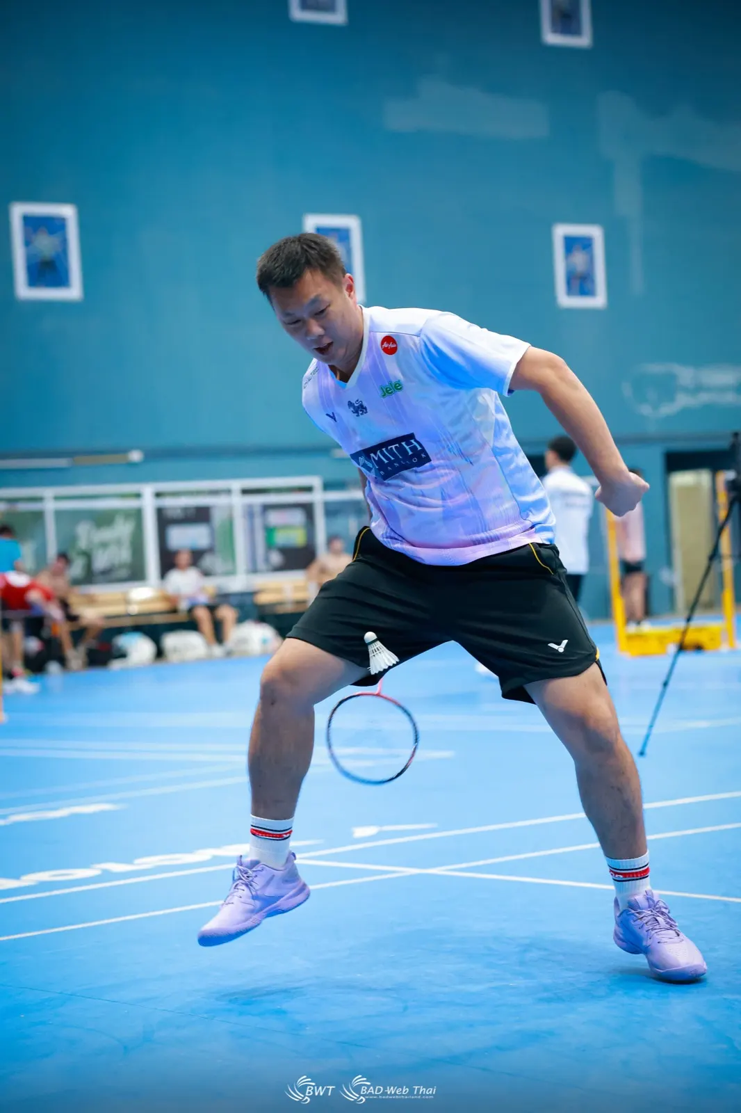 Joueur en position basse, jambes fléchies et raquette devant, prêt à réagir au badminton
